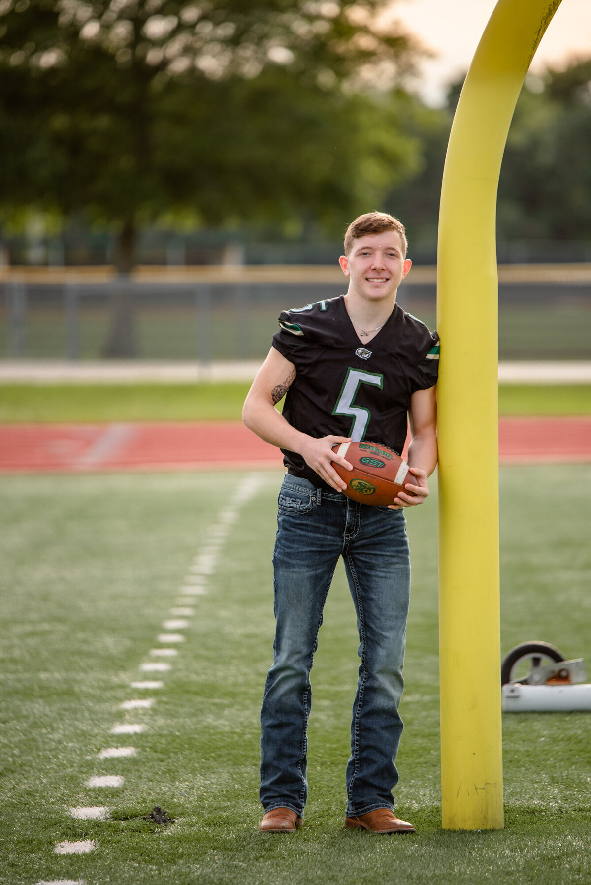 A senior boy leans against a field goal post at his high school football field.