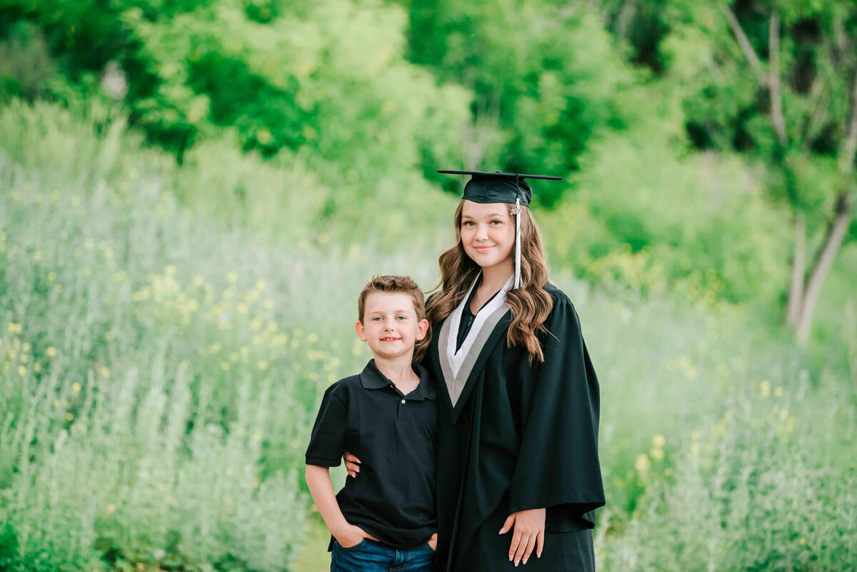 Wearing her grad gown and cap, standing with her brother. 