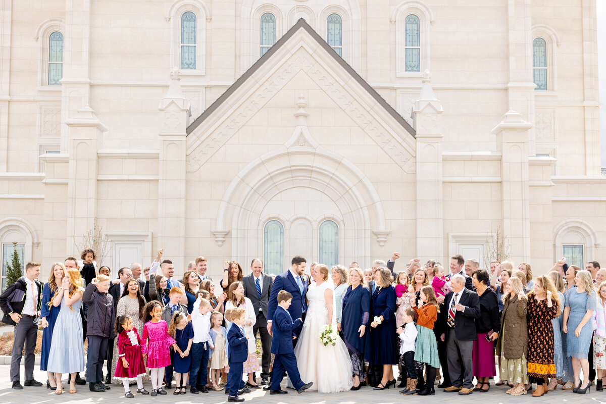 Close-up of the wedding party smiling and celebrating with the bride and groom centered, with the temple’s elegant stonework in the background.