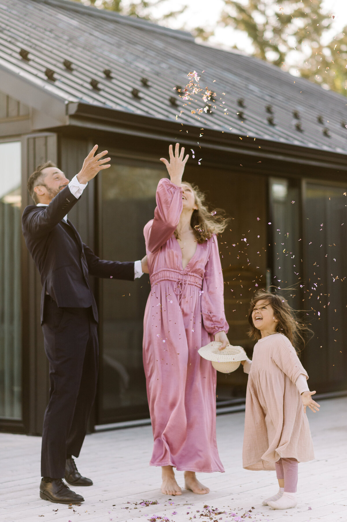 A joyful couple and their daughter tossing confetti in the air on a porch at Wander The Resort after they eloped