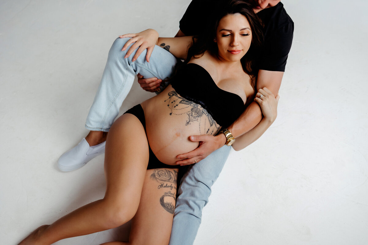pregnant mom wears black bra and underwear while husnand holds her belly