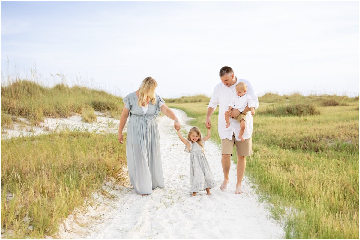A family of four holding hands walking through the sand dunes