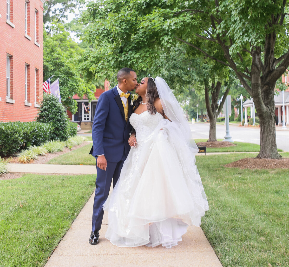 groom wearing blue tux kissing his bride wearing a white dress and veil