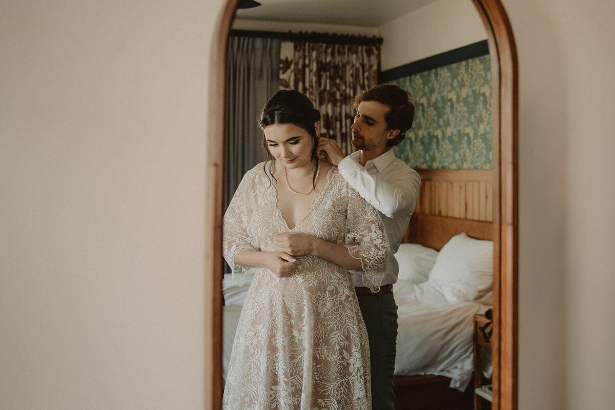 Someone helping their partner put on a necklace on their wedding day 