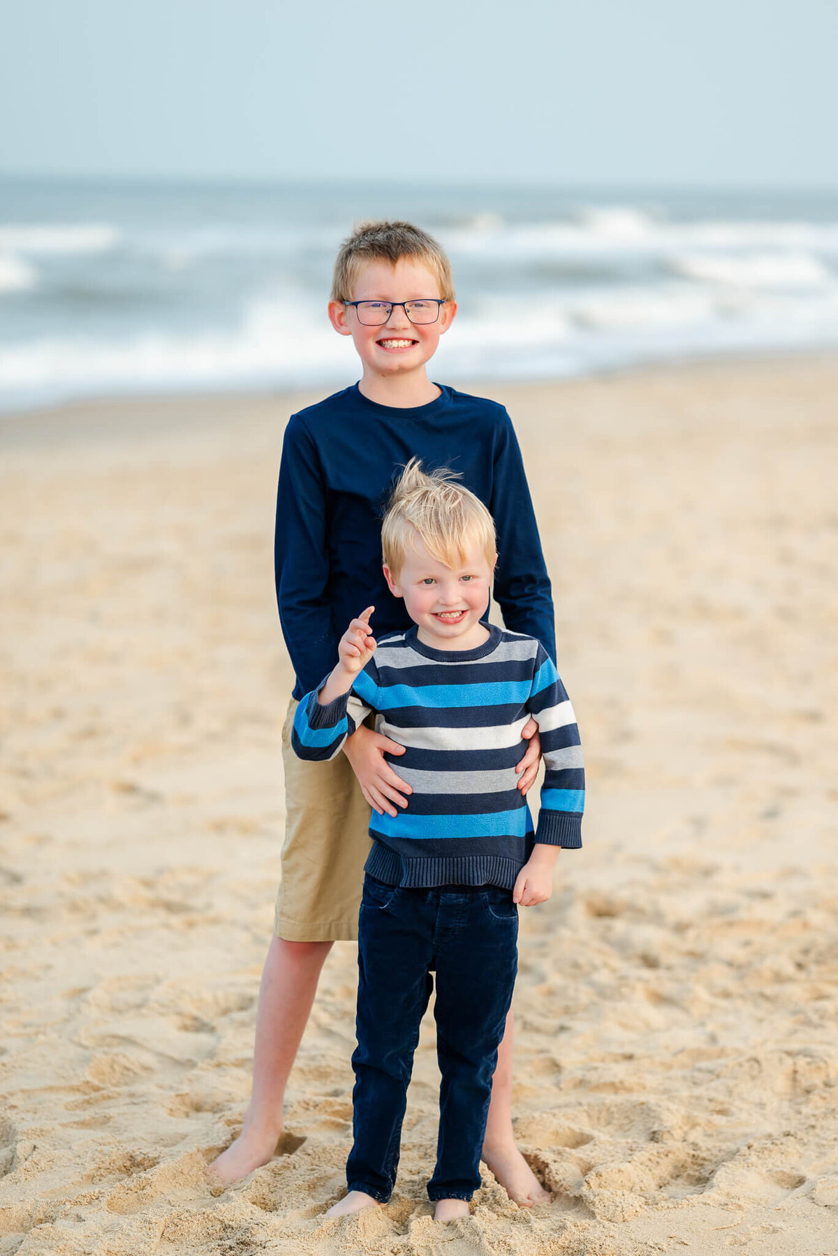 Justine Renee Photography captures a picture of two brothers in front of the  water at the beach in Norfolk, Virginia. The boys are all smiles for the photo.