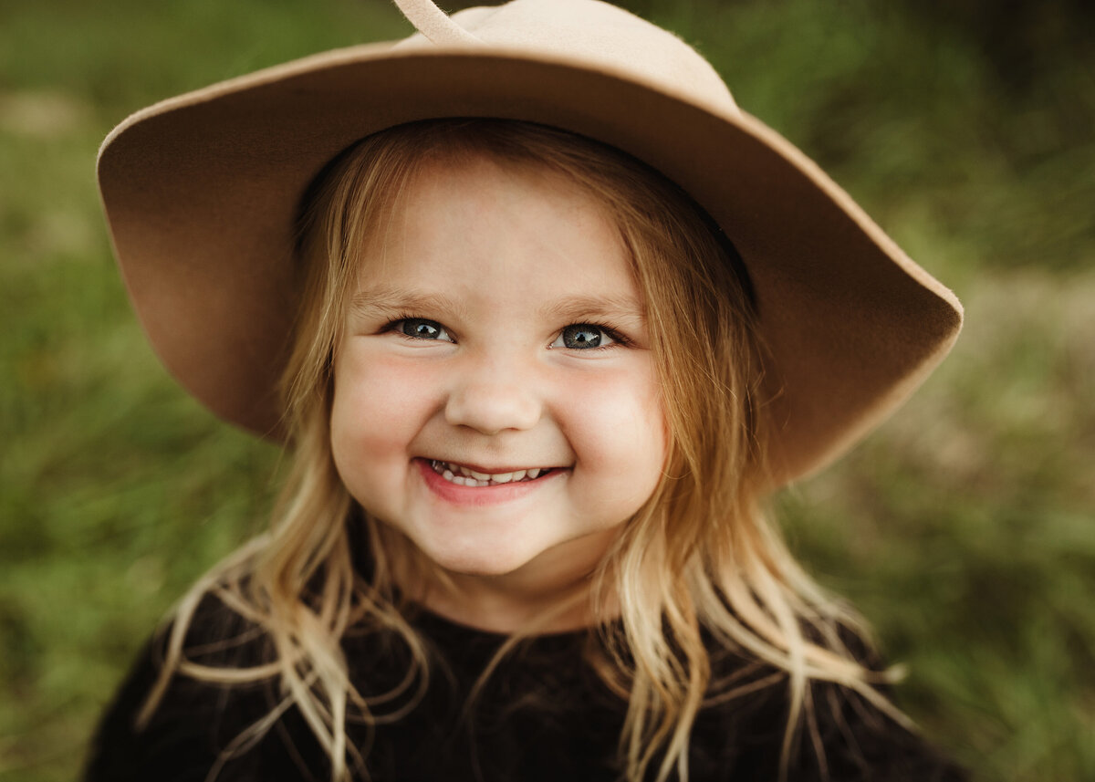 A little girl wearing a sun hat is grinning.