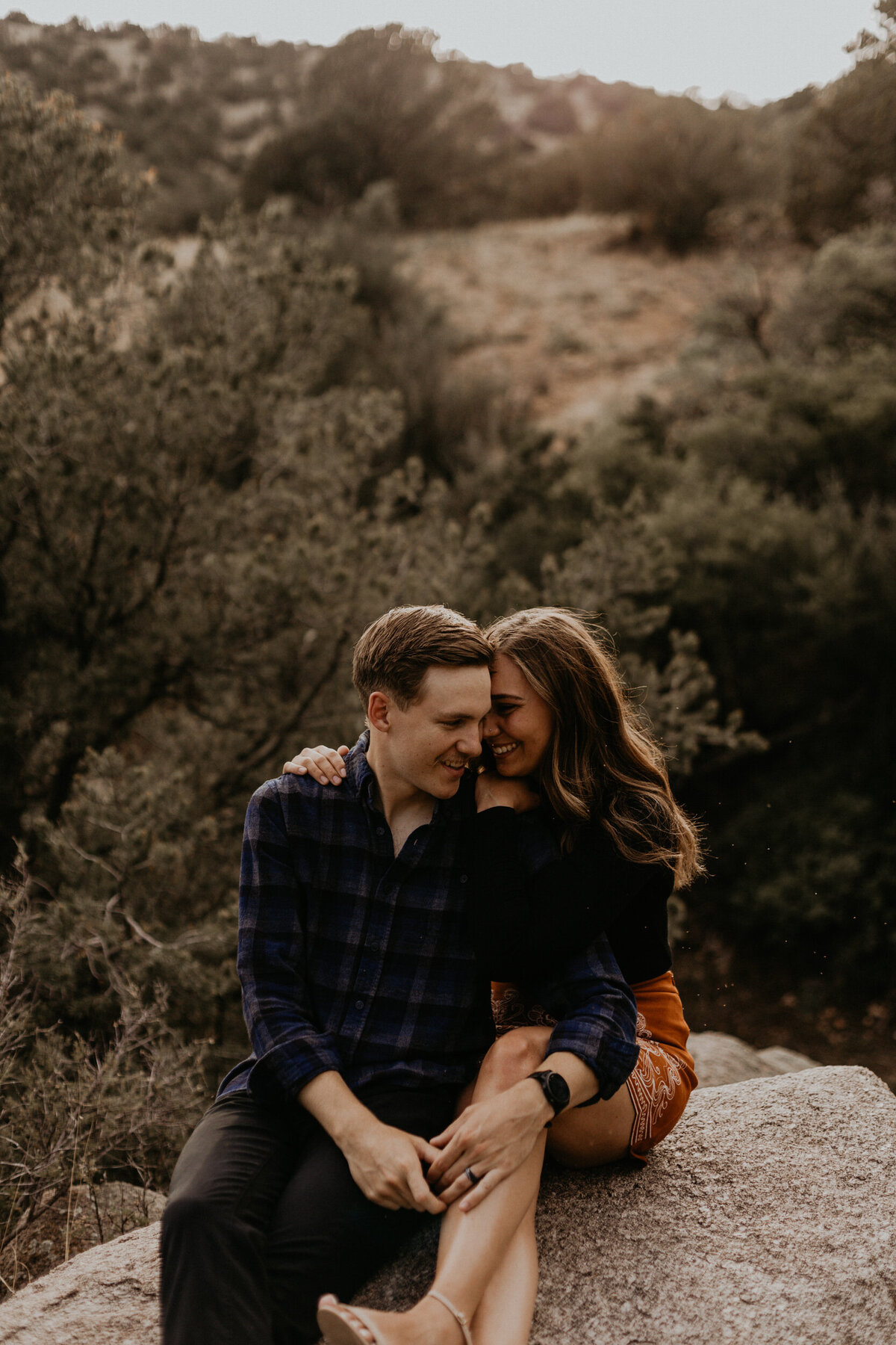 engaged couple sitting on a rock together laughing
