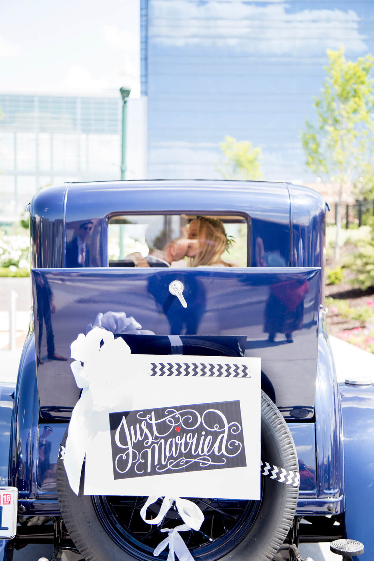 a blue vintage car with a just married sign and a couple kissing in the window