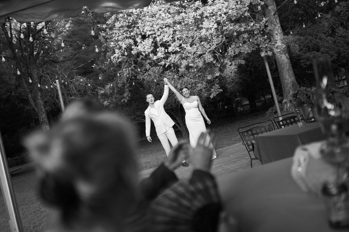 A bride and a groom holding hands celebrating looking at their guests after their first dance. 