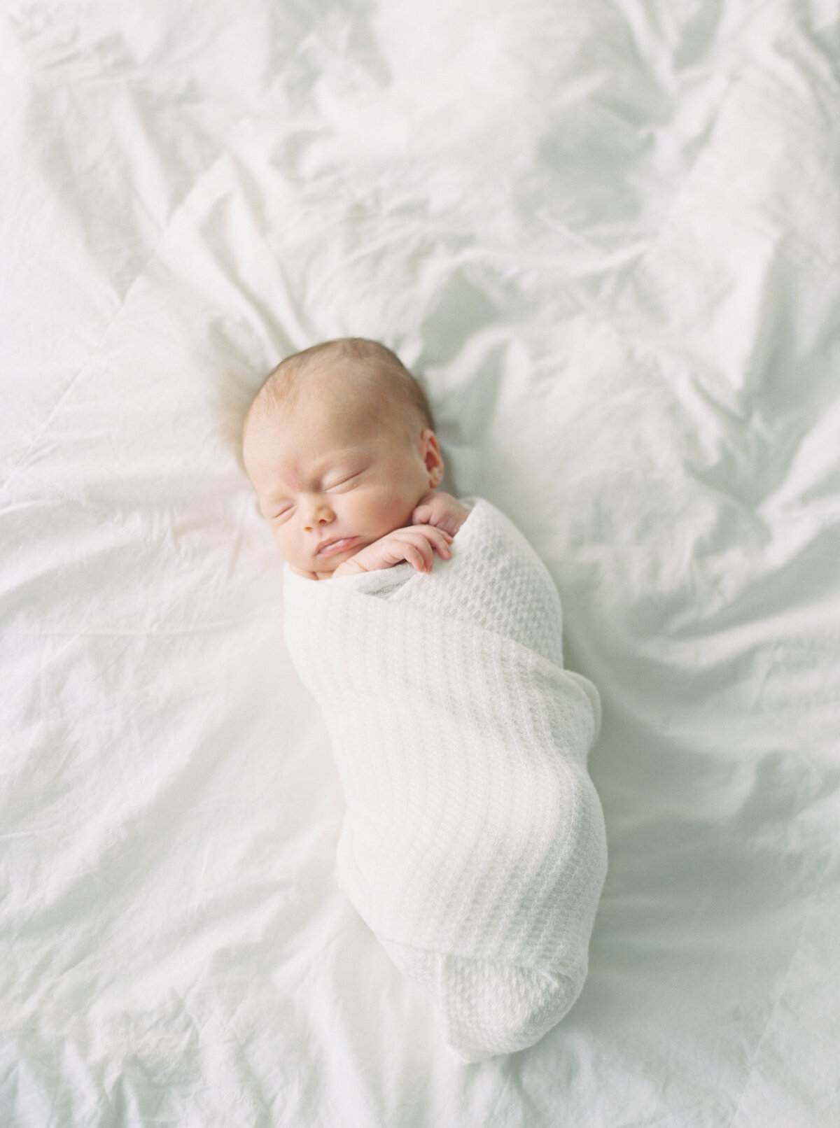 newborn baby girl in all white on master bed by photographer in madison wi talia laird photography