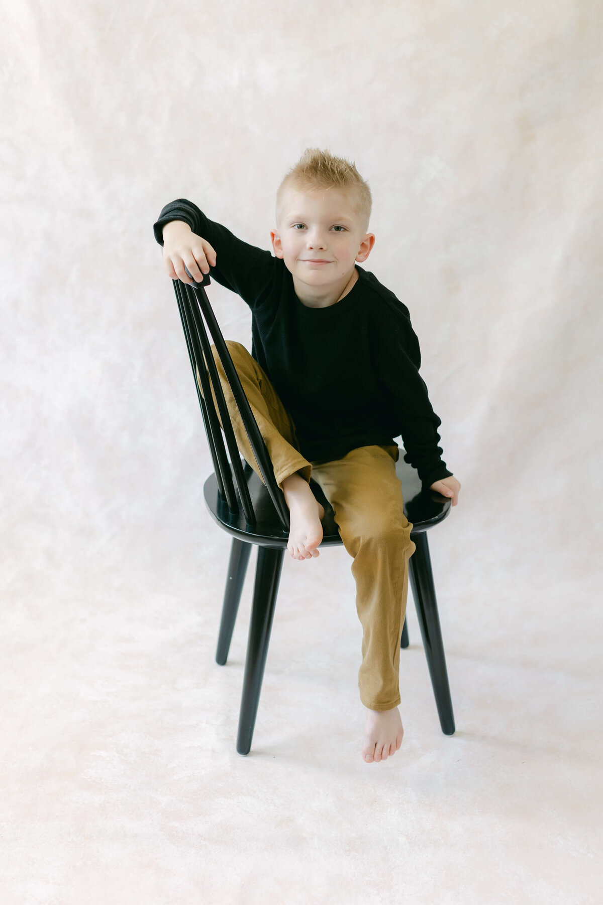 A young boy smiles while sitting in a black chair.