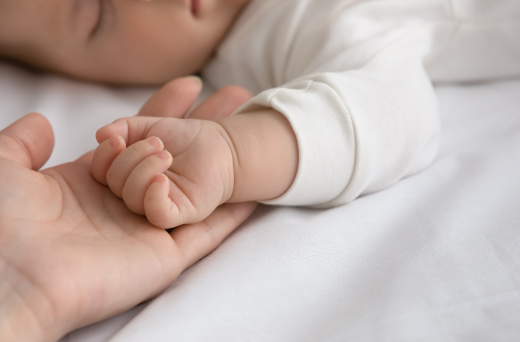 A heartwarming moment at our postnatal retreat as a baby peacefully rests in a white cradle while mom gently holds his little hand with love and tenderness.