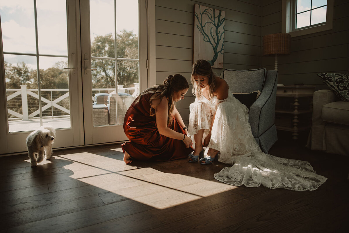 Someone helping someone in a wedding dress put on shoes