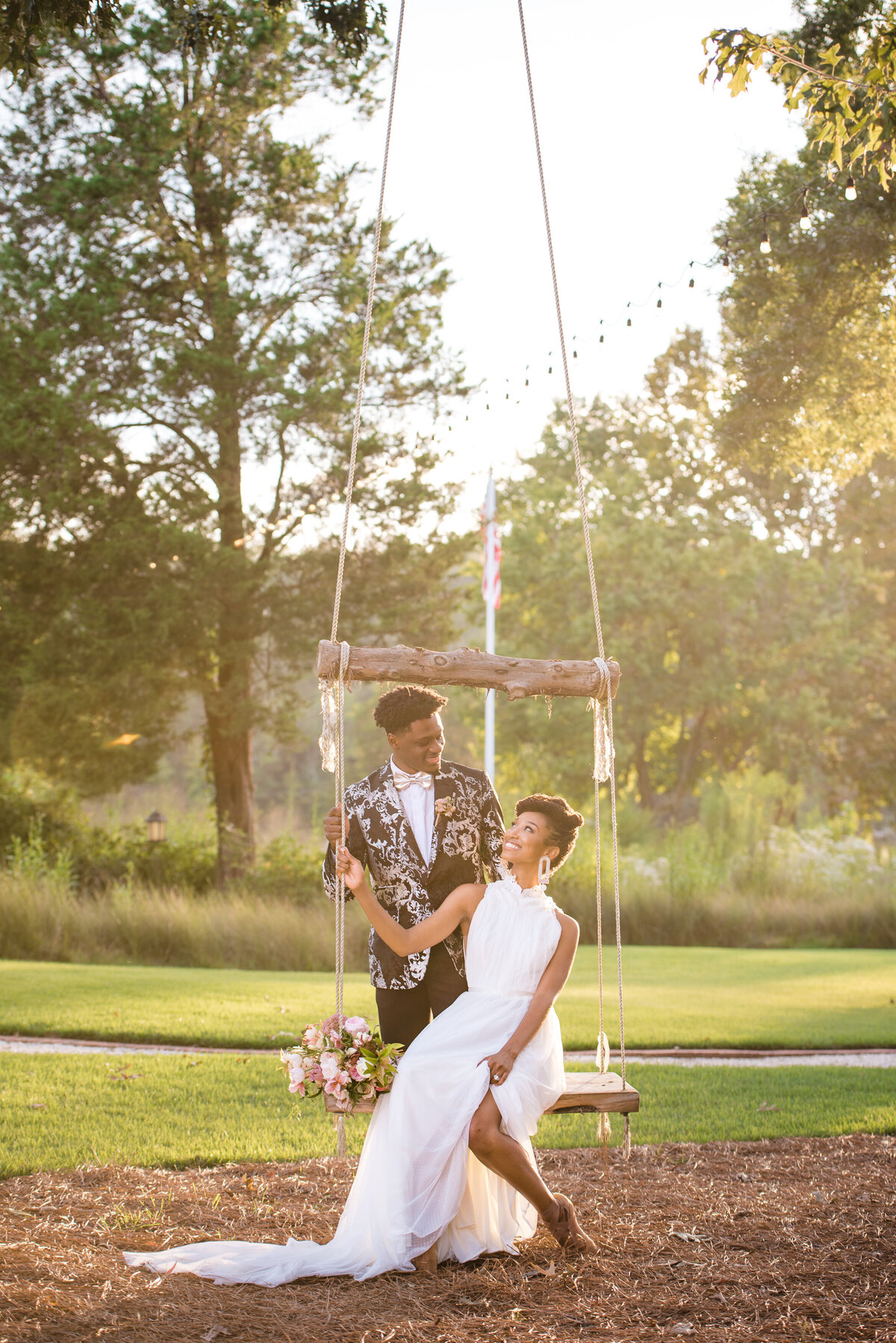 Black bride sitting on the swing at North Cover Haven looking back at her groom  who is standing behind her both smiling by Charlotte wedding photographers DeLong Photography