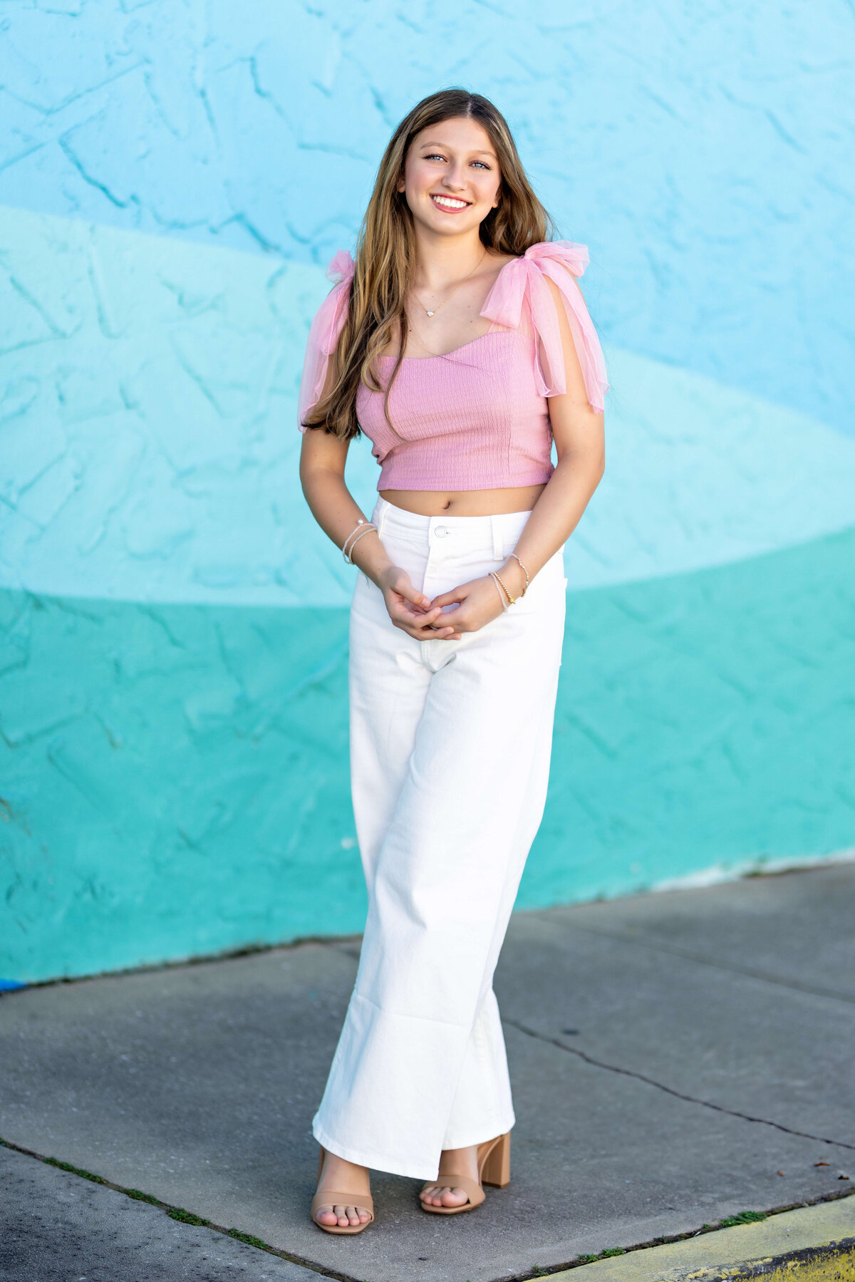 Senior girl posing in front of a blue wall with pink top in Windermere, Florida