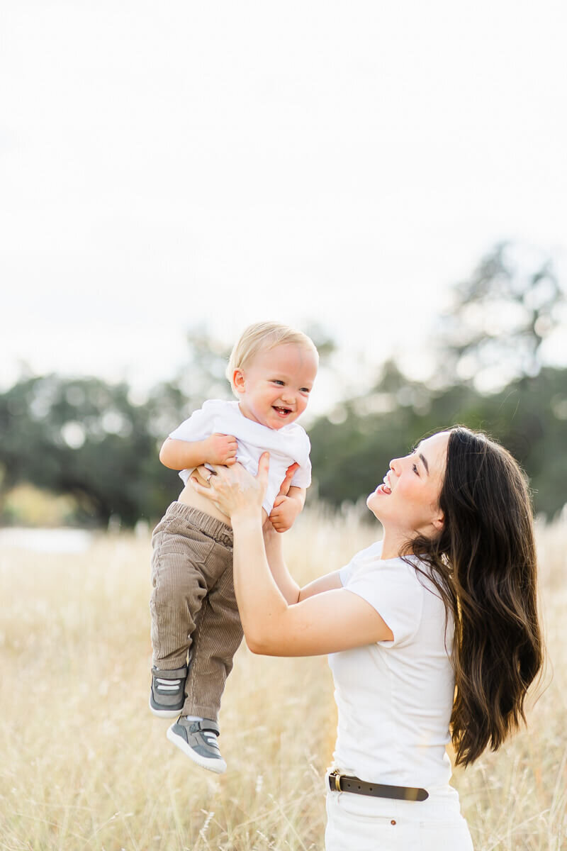 a mother lifts her toddler son up in the air while he laughs during their family photo session.