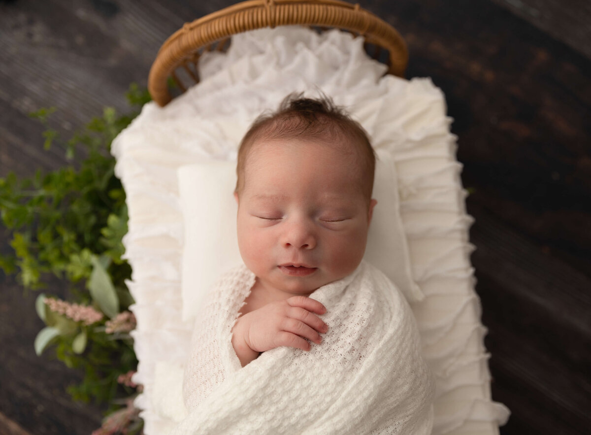 Photo of a newborn wrapped in white in a bed in an Erie Pa photography studio