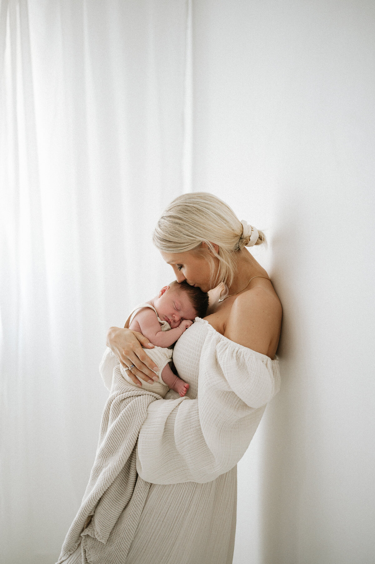 Mother cuddles her sleeping baby against a white wall