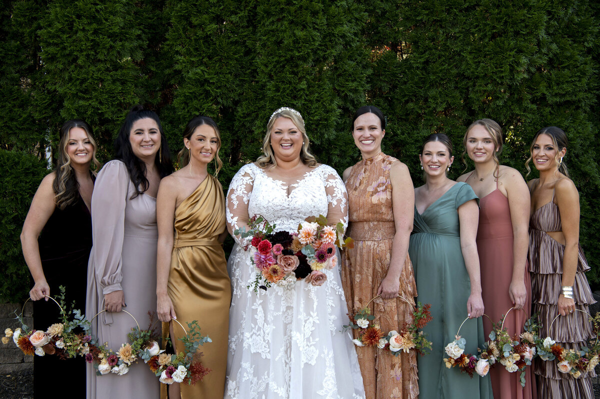 A newlywed in a dress smiling with their wedding party on either side of them 