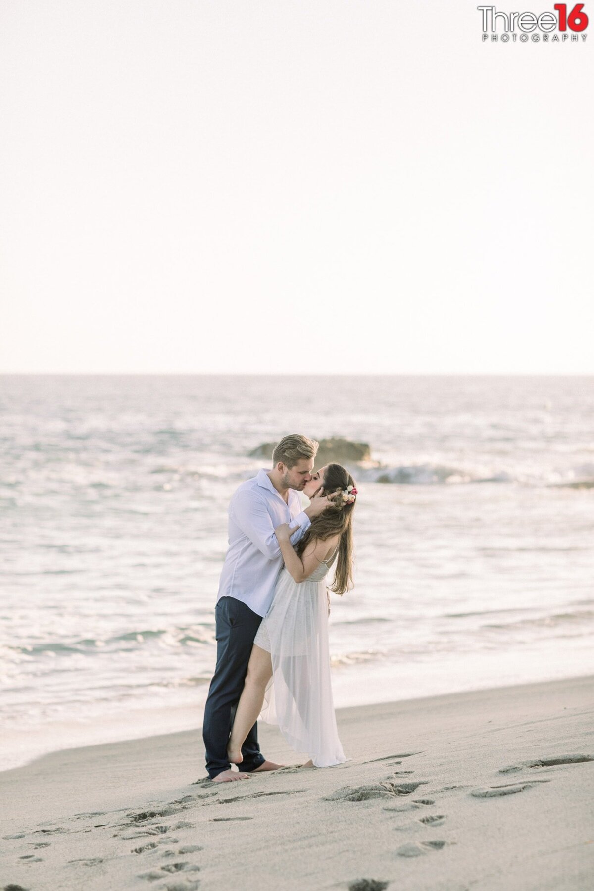 Newly eloped couple share a kiss on the sandy beach near the ocean