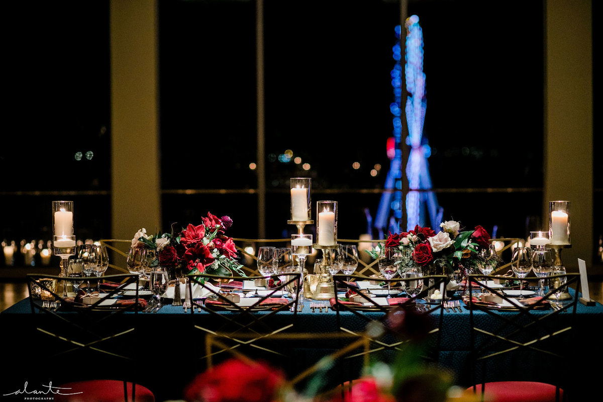 long reception table with red chairs, blue linen, and Seattle ferris wheel in background