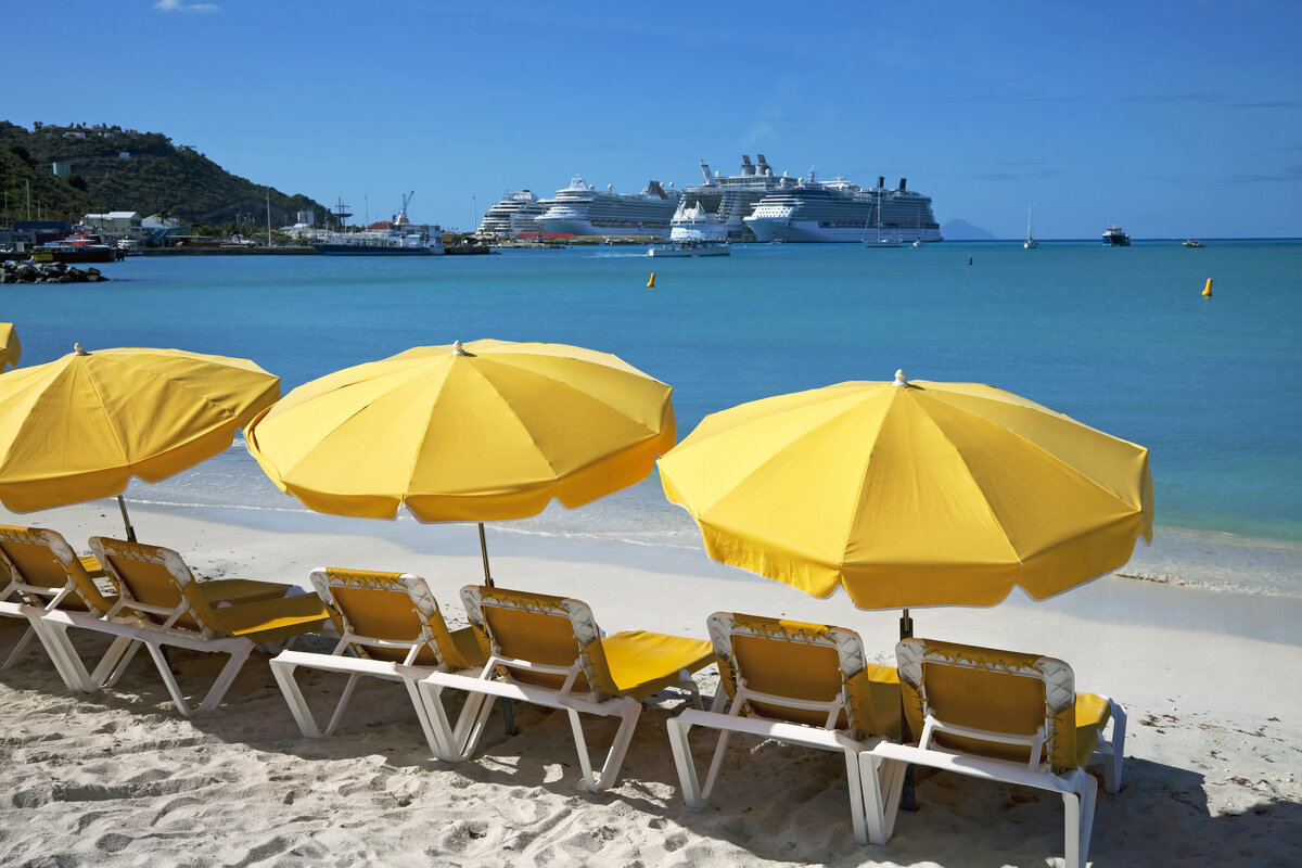 A serene beach with yellow beach chairs and umbrellas facing the ocean with cruise ships in the distances.
