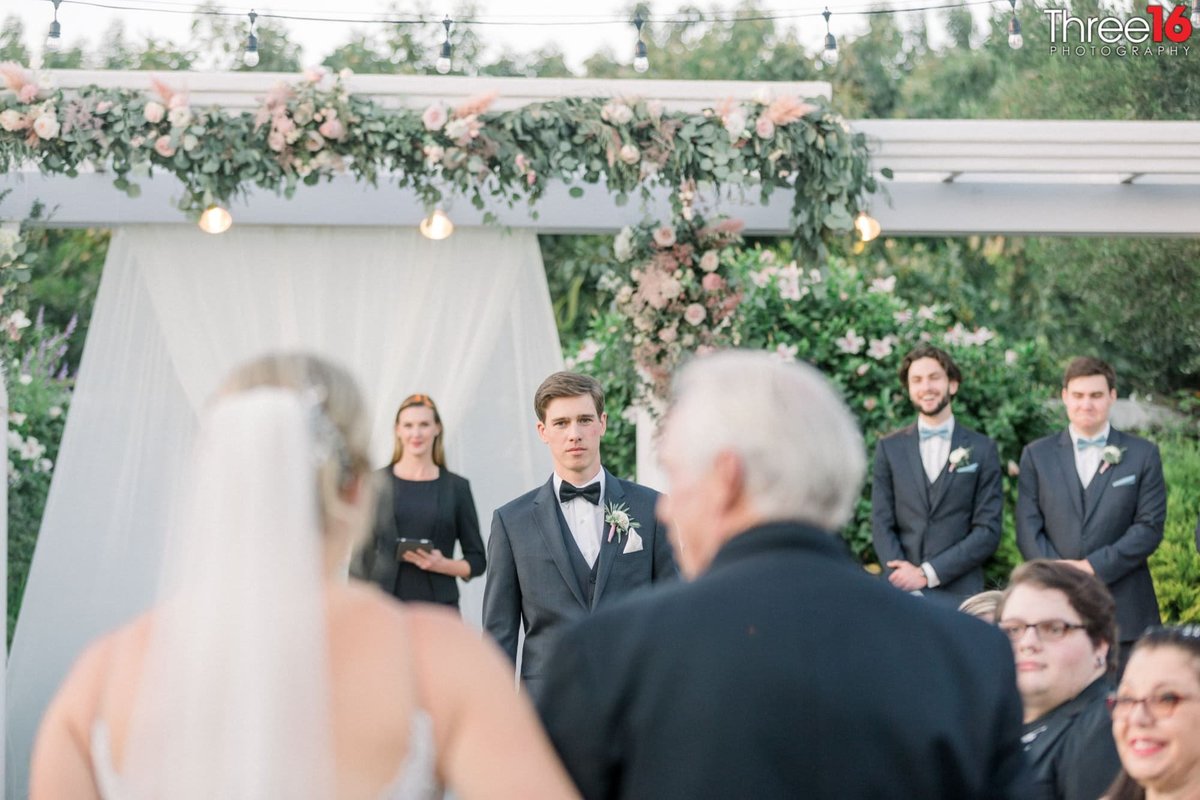 Groom stands at the altar as the Bride is being escorted up the aisle by her father