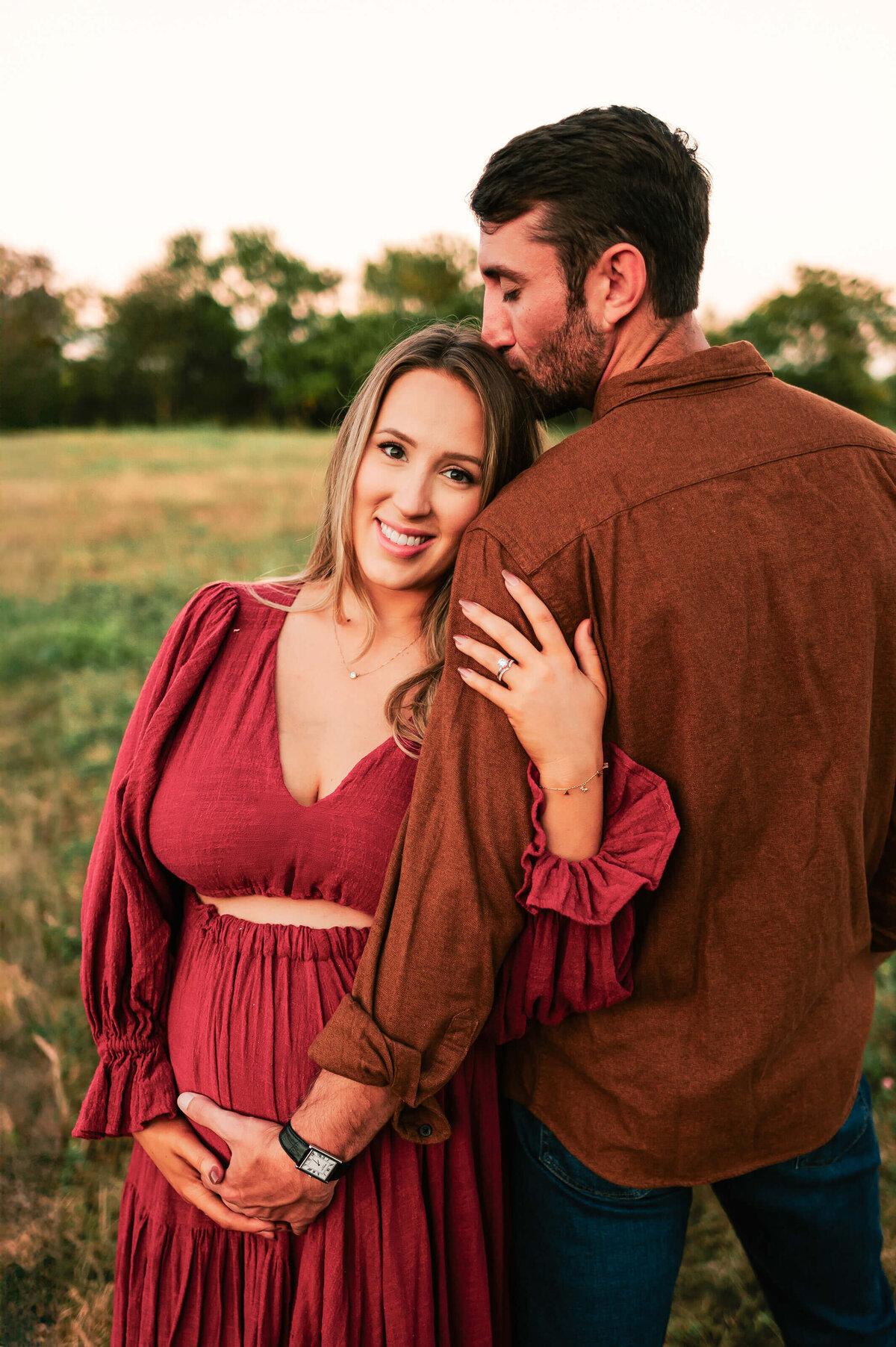 Springfield MO maternity photographer captures pregnant mom hugging husband at sunset in a field