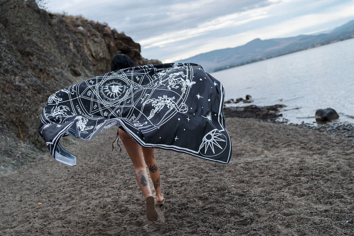 woman astroligist running with blanket on beach for creative photoshoot