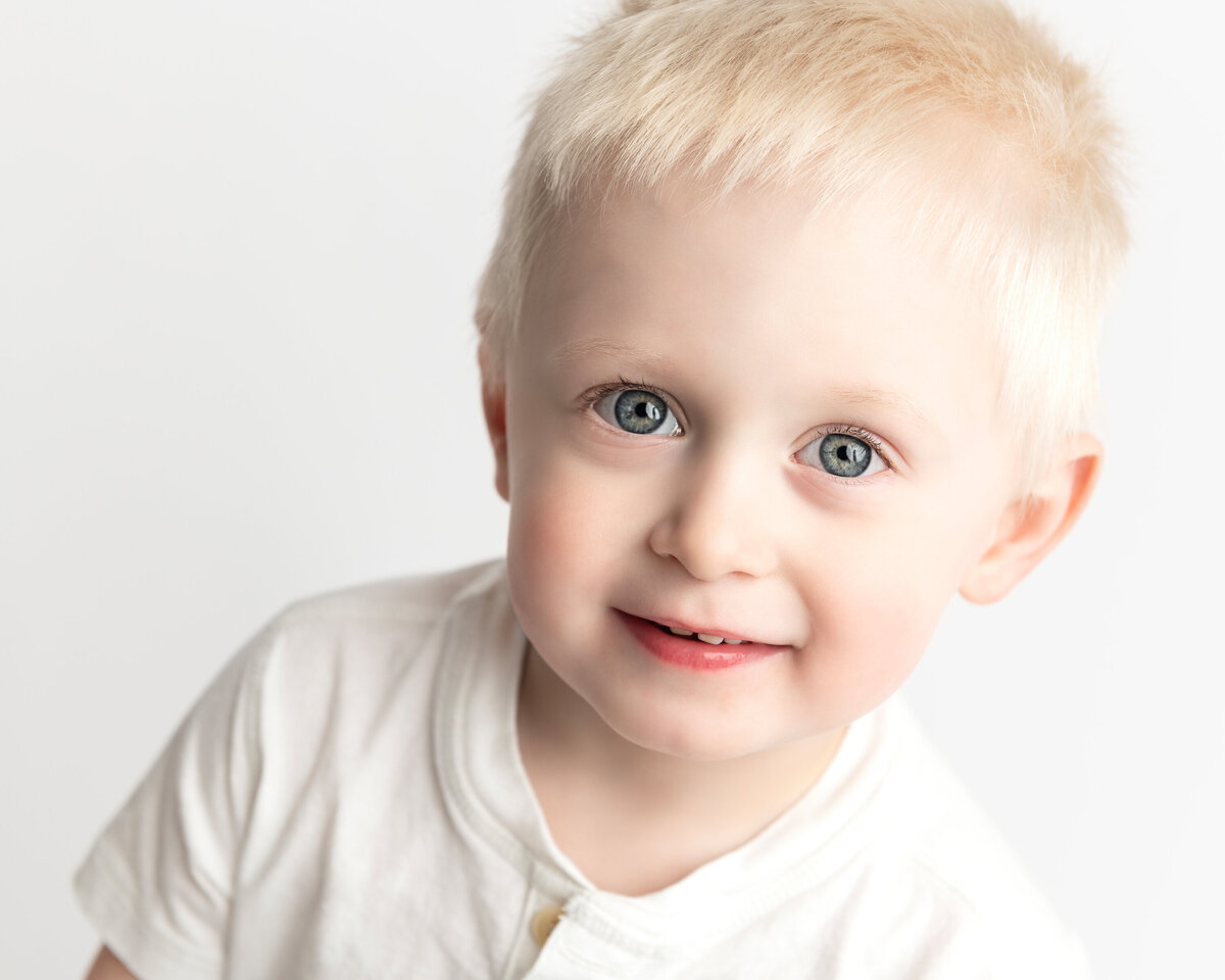 Personality portrait of a smiling toddler boy in white shirt—captured with playful warmth in studio light.