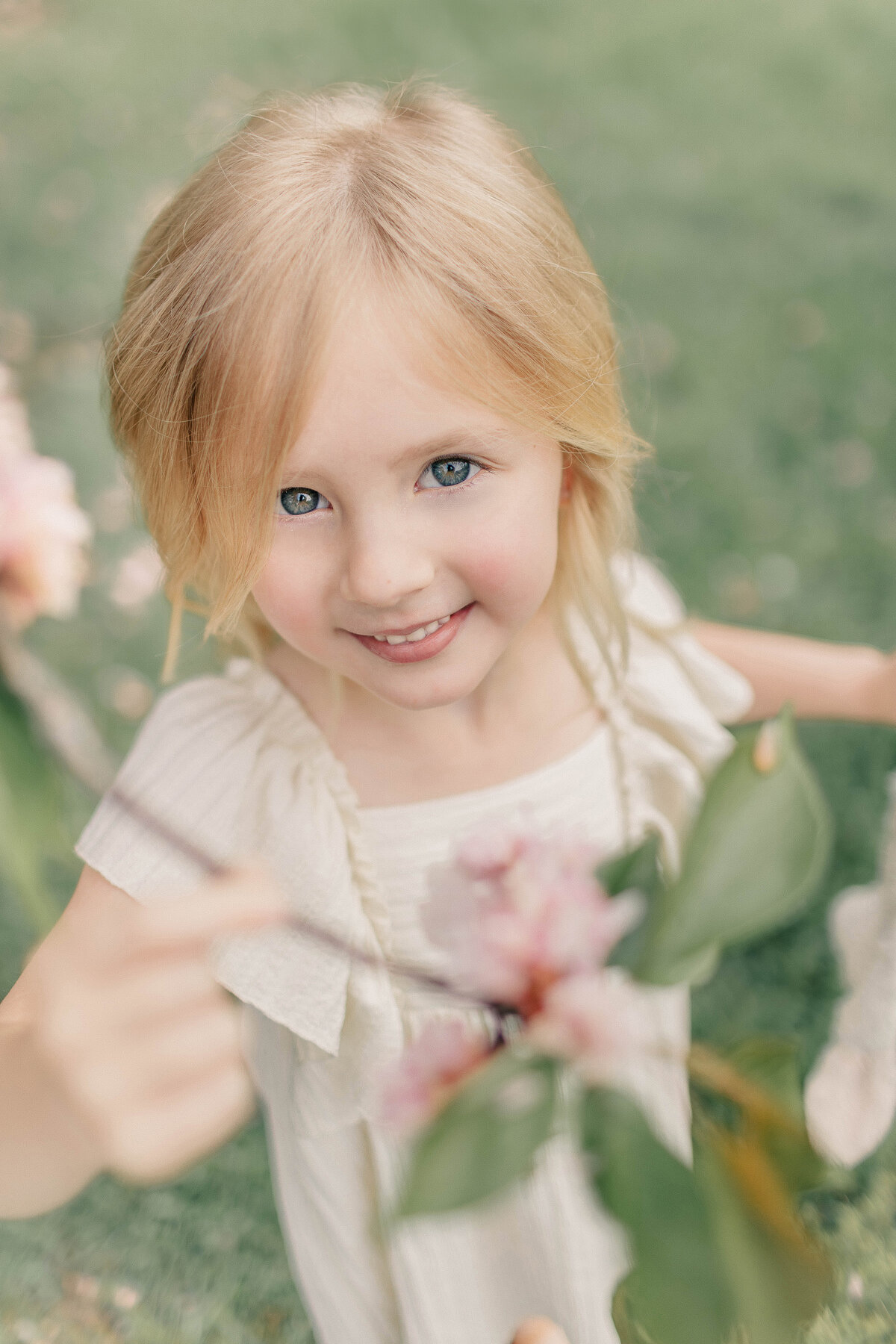 Young girl smiling beside a pink flower branch during a Mommy and Me maternity session in a Kansas City park.