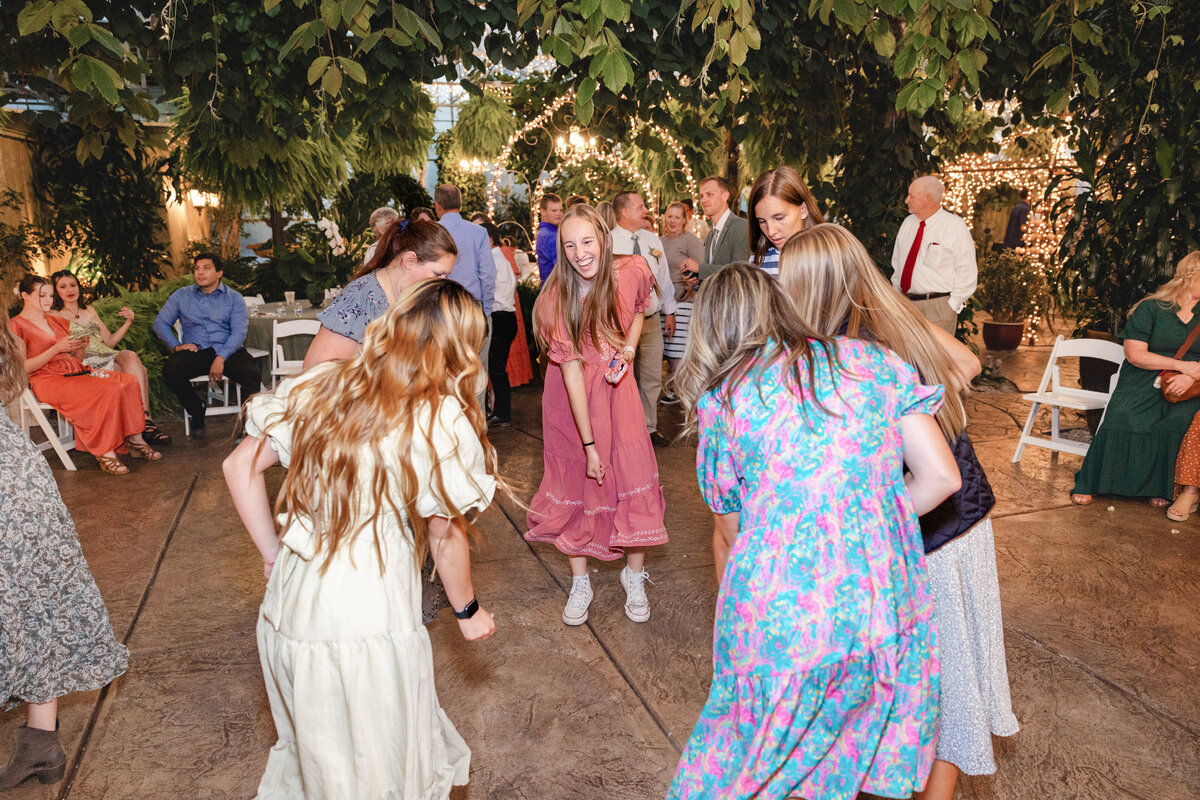 Wedding guests laugh and dance beneath the lush foliage and string lights of Le Jardin’s enchanting reception space.