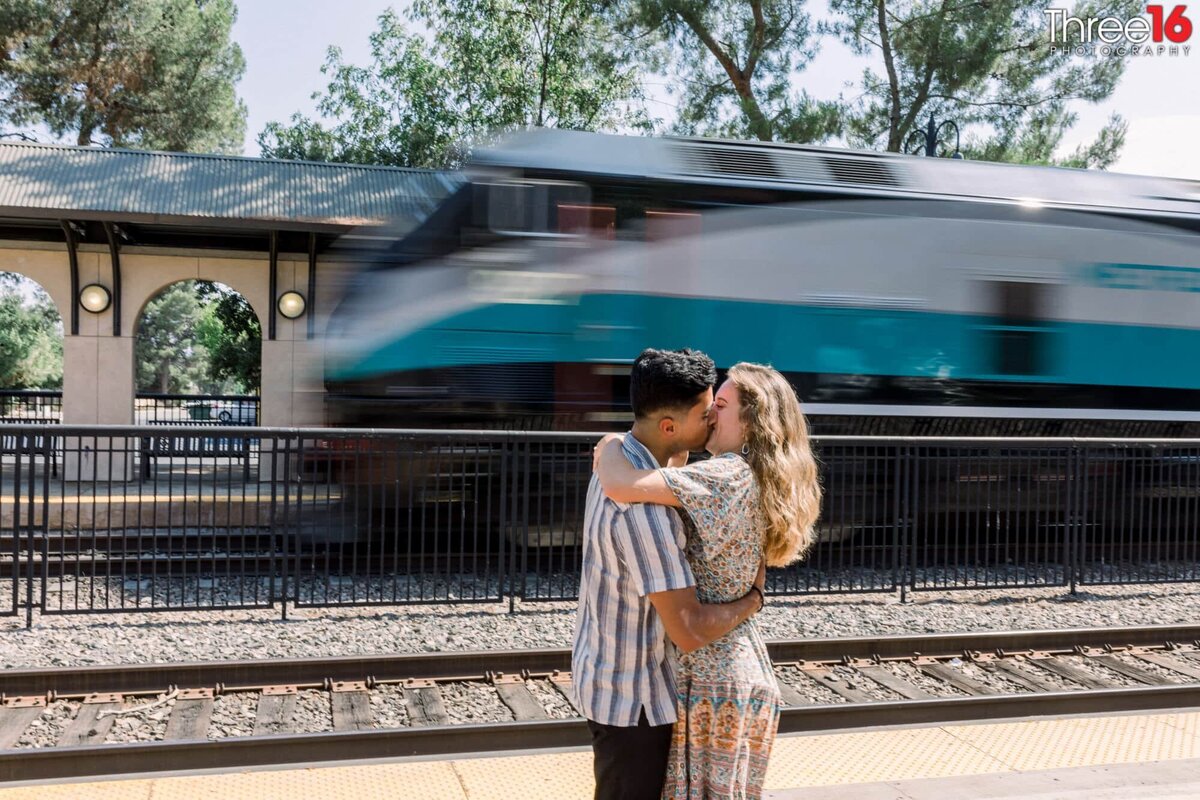 Engaged couple stand along the train tracks as the trains goes by at the Claremont Train Station