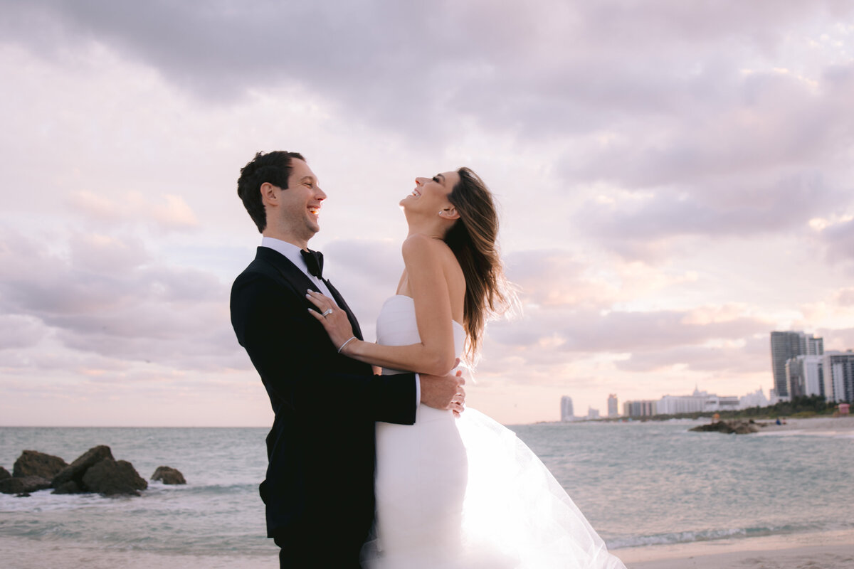 Bride and groom laughing together on the beach at sunset, captured by Rodrigo Varela Photography.