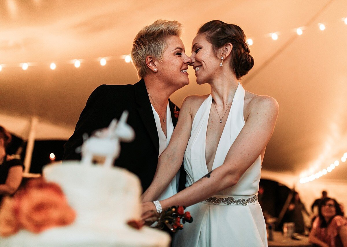 two brides cutting wedding cake with unicorn cake topper and orange flowers