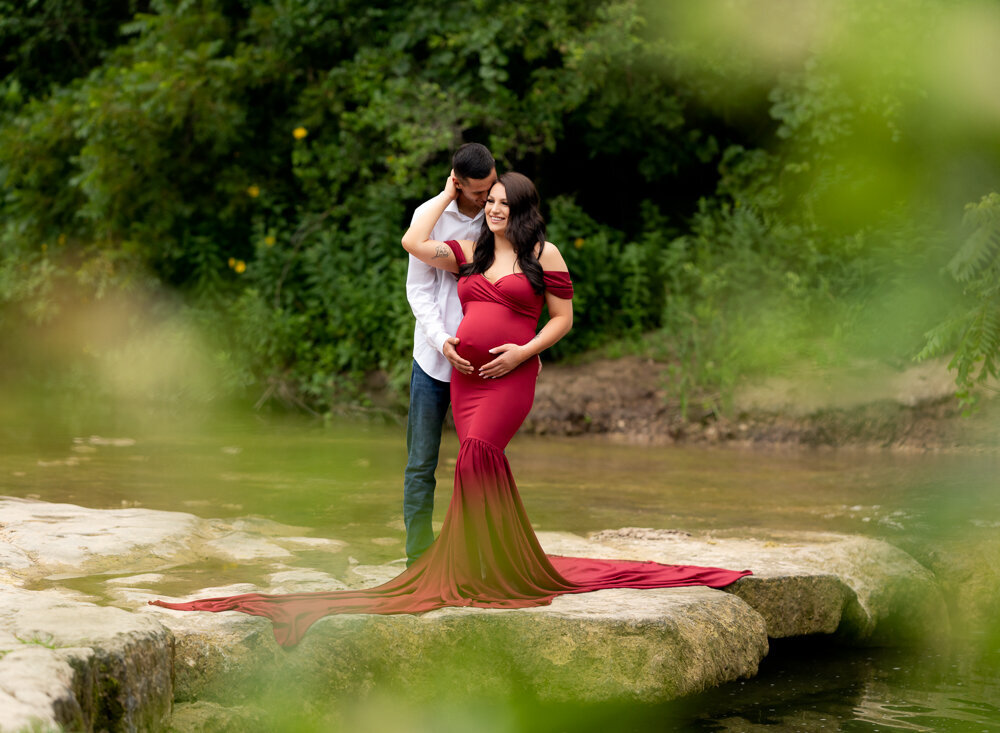 Romantic maternity photo of expecting couple standing on rock by the river in Georgetown, TX