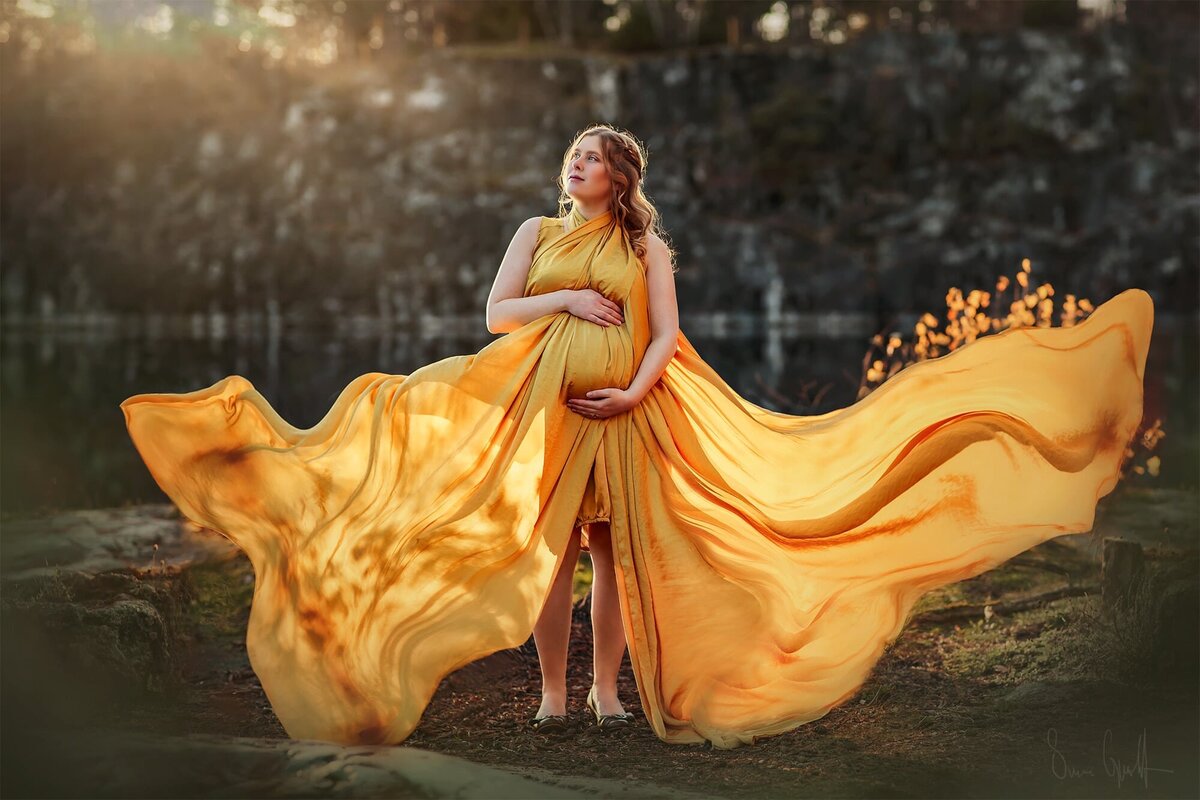 gravidfotografering vid ett vattenfyllt stenbrott med gyllengul svävande klänning