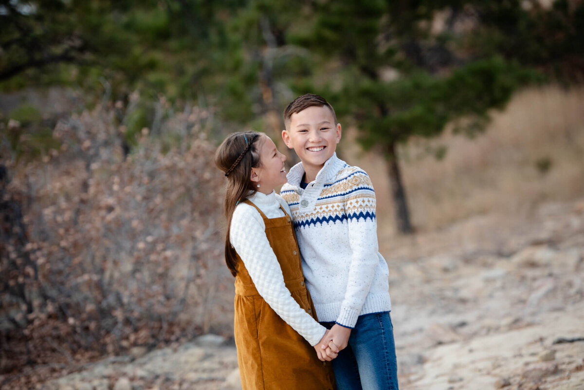 A brother and sister laugh while hugging and holding hands in a mountain trail