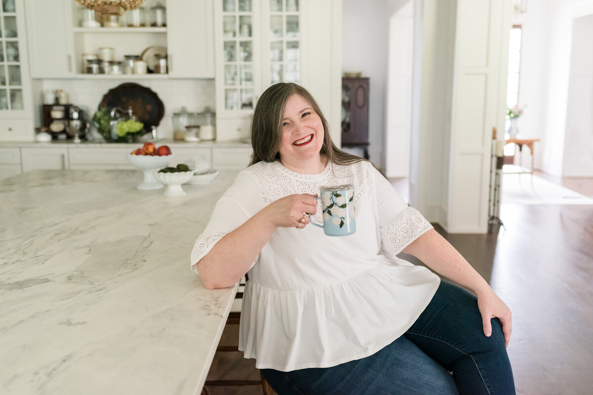 Lauren sits on a stool next to her kitchen island drinking coffee out of Rifle Paper Co. floral mug