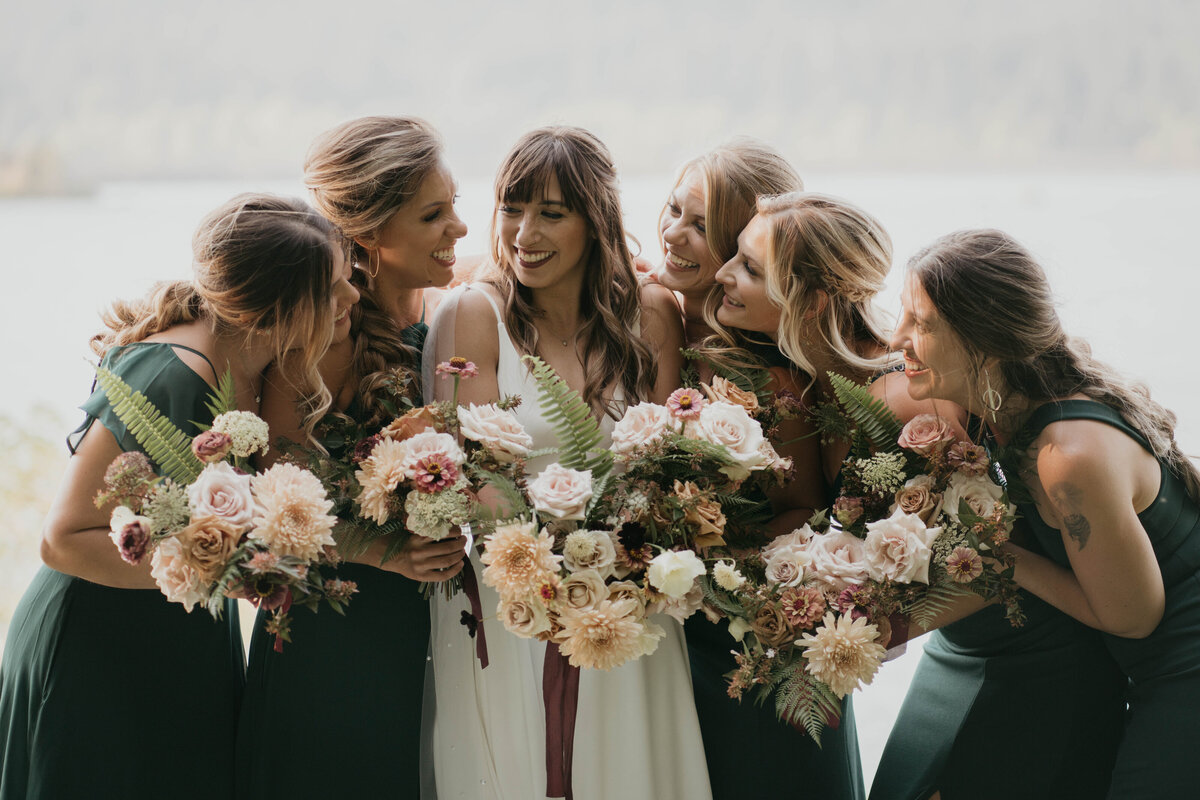 bride and bridesmaids in green dress looking and each other and smiling
