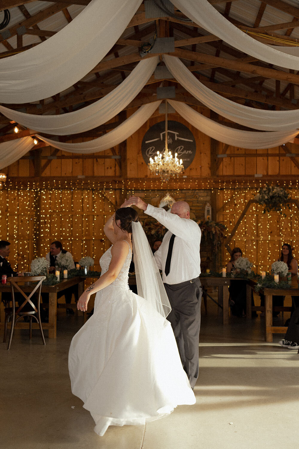 Father-daughter dance in a warmly lit, rustic barn with fairy lights