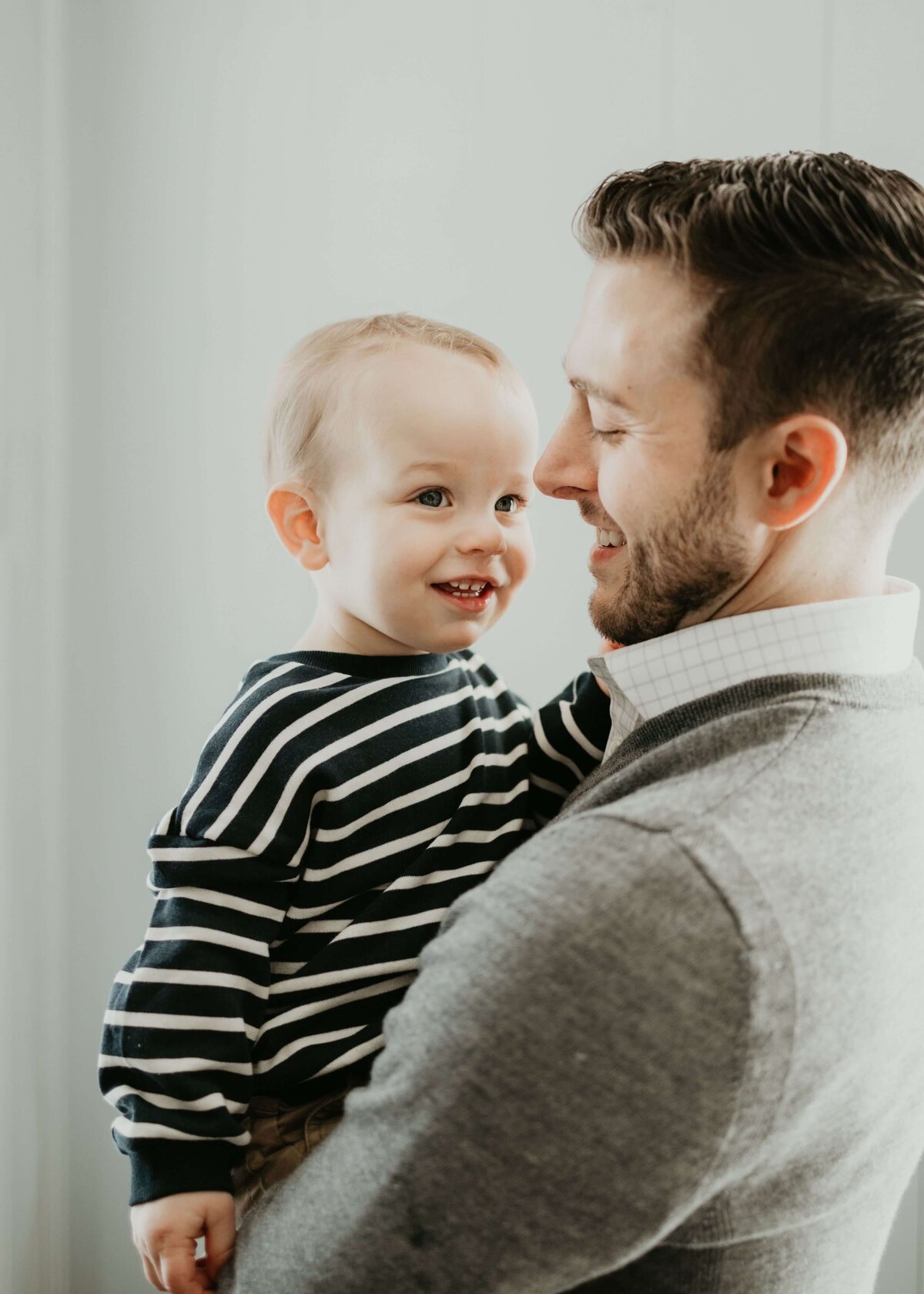 A Pittsburgh family photographer captures a man holding a baby boy in front of a white wall.