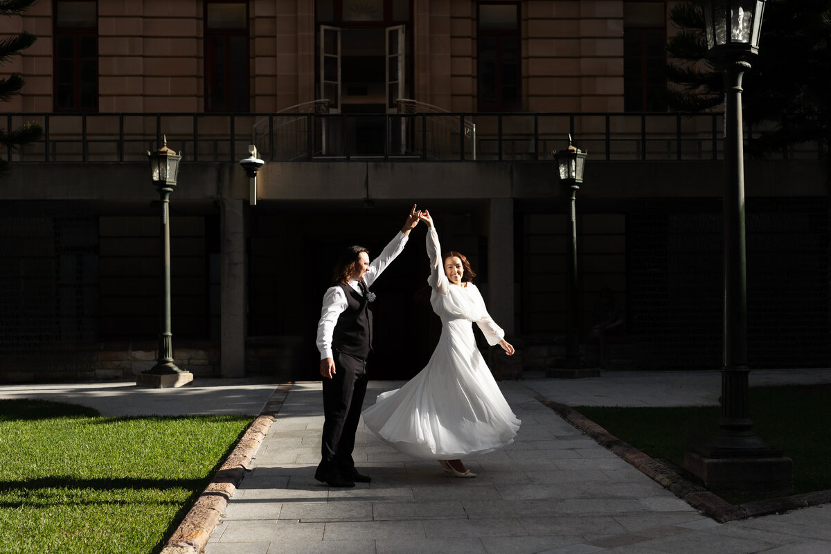 Newlyweds dancing in a sunlit path at Anzac Square Brisbane during their registry office wedding celebration.