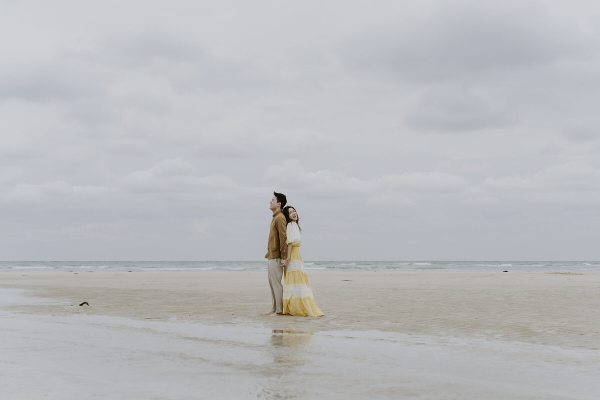 the couple posing back to back in the shore of jeju island