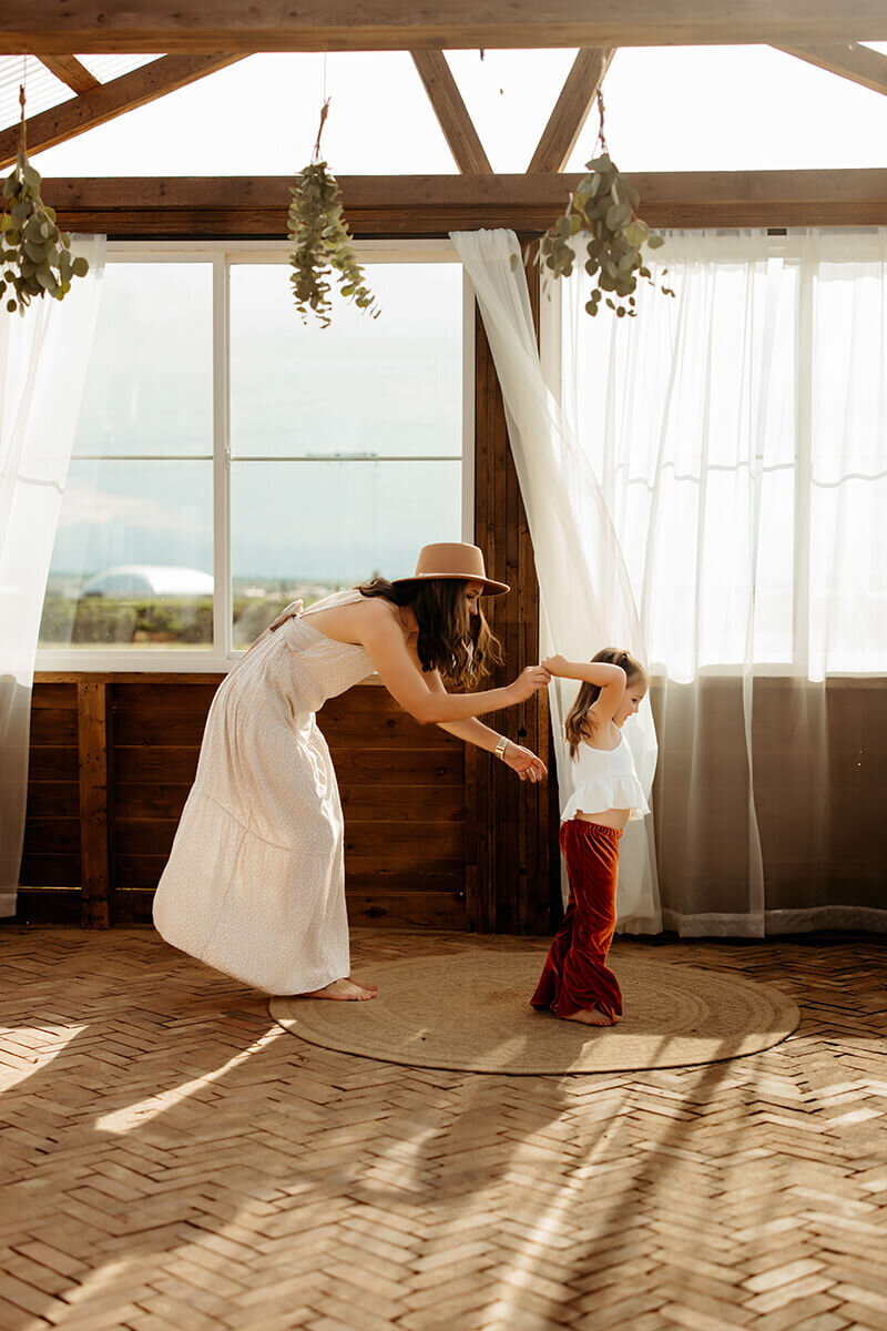 Mom holds hands and dances with toddler daughter in a brick greenhosue
