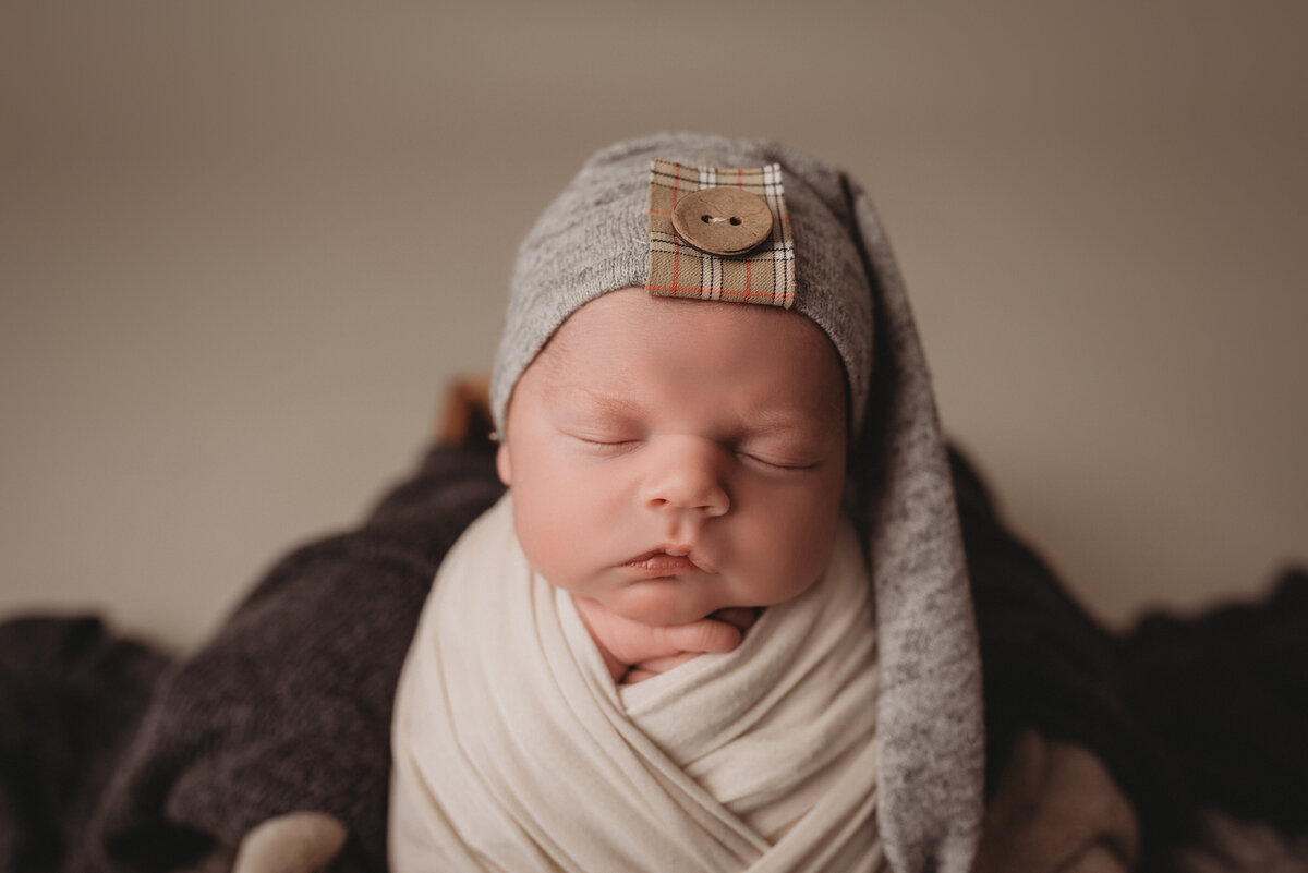 2 week old baby boy at atlanta's best newborn photography studio posed in a cream swaddle wrap sitting in a woven basket with creams and greens