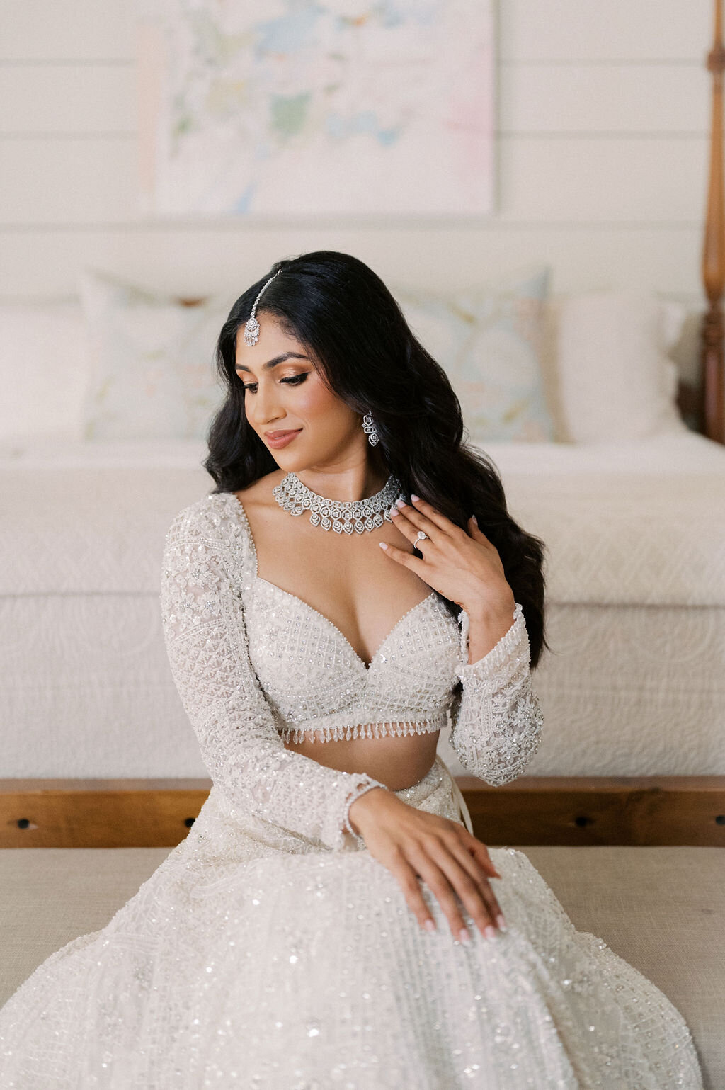 Bride in a beaded gown adjusting her necklace during getting-ready portraits.