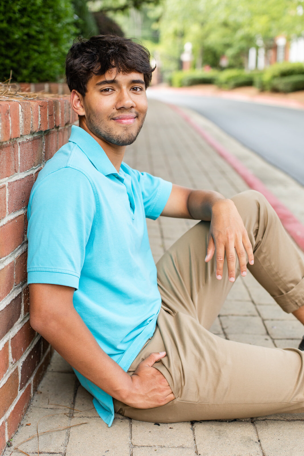 Senior boy sitting on the sidewalk wearing beige pants and blue shirt Spring photo session Laure Photography