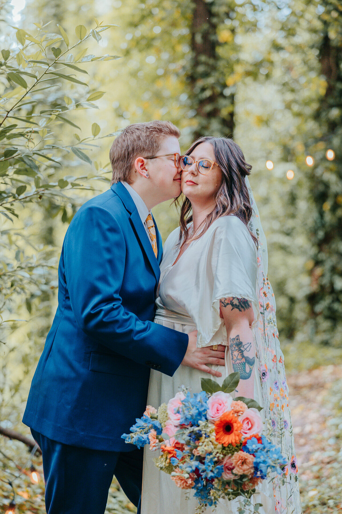 LGBT newlyweds snuggle in a forest while holding a colorful bouquet