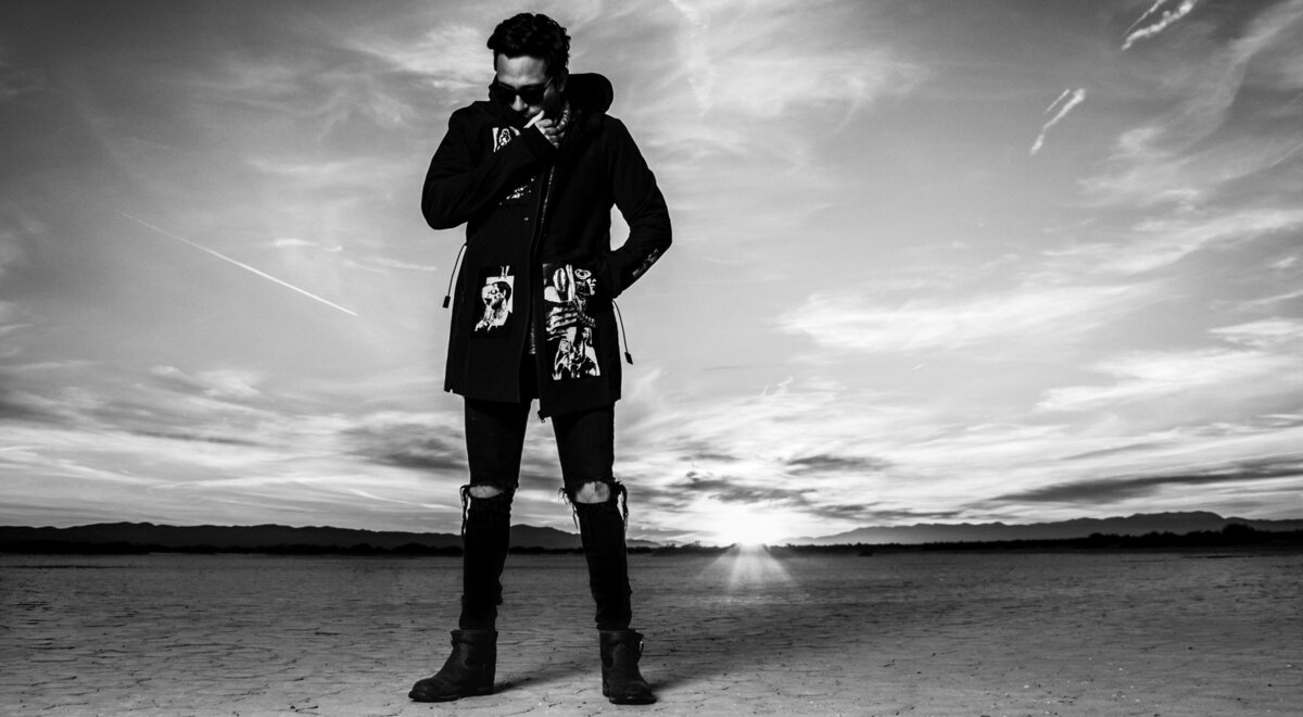 Black and White Musician Portrait Dagg3rs Sunger standing in desert sun setting behind him covering nose and mouth with collar of jacket wearing sunglasses El Mirage